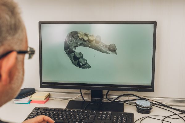 Figuras 3D, hombre mayor con anteojos realizando la revisión de un prototipo digital en 3D que muestra la mandíbula de un animal desconocido, el modelo 3D que se va a imprimir para unirlo en una figura se va a utilizar para una adaptación dentro de la industria del entretenimiento. Es necesario realizar estos modelos digitales antes de imprimir para tener una idea previa de lo que posteriormente se montará en la figura 3D final. El hombre se muestra concentrado y comprometido a realizar un trabajo de calidad en el prototipo digital, ya que eso se considera como una parte importante del proceso. 